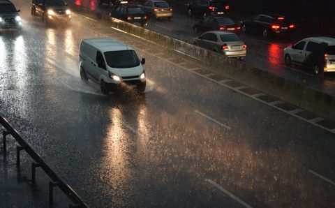 Vehicles driving through heavy rain on a wet road at dusk