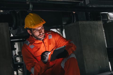 A site worker in overalls records information on a tablet