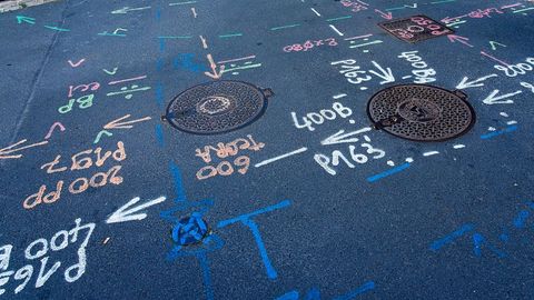 Utility survey markings on a road surface, next to manhole covers