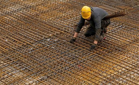 A worker fixing steel reinforcement bars across a large construction slab