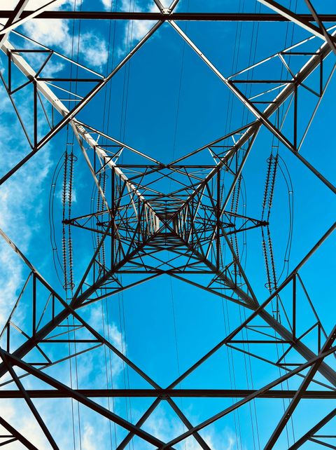 Looking up through the lattice of an electricity transmission tower against a blue sky